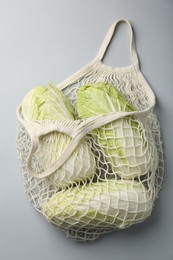 Photo of Fresh Chinese cabbages in string bag on light background, top view