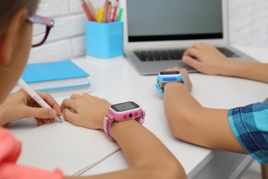 Photo of Children with stylish smart watches at white table, closeup