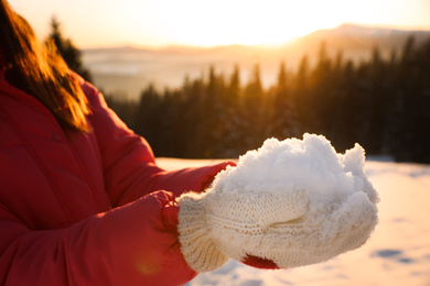 Woman holding pile of snow outdoors, closeup. Winter vacation