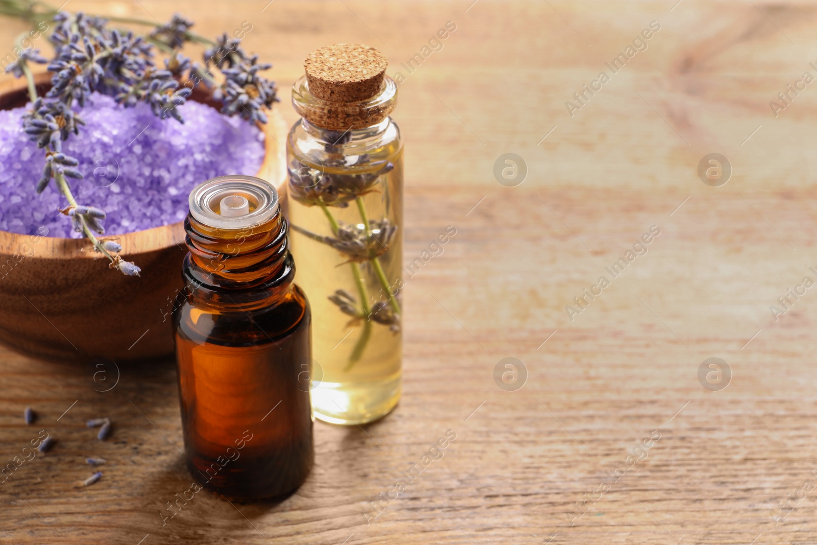 Photo of Bowl of sea salt, essential oil and lavender flowers on wooden table, space for text