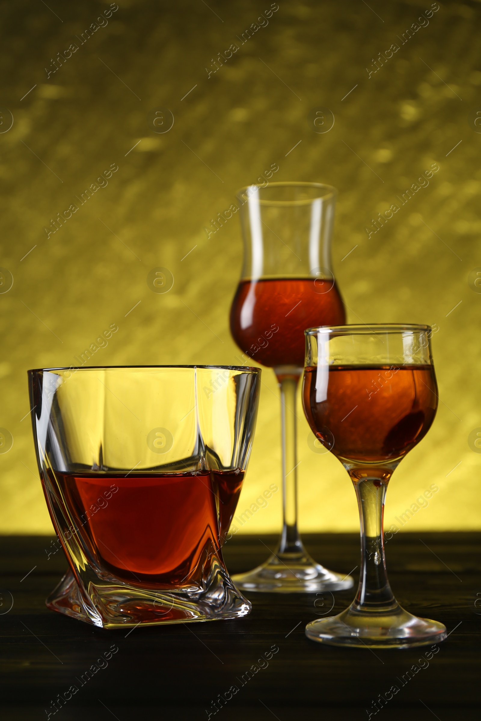 Photo of Different delicious liqueurs in glasses on dark wooden table