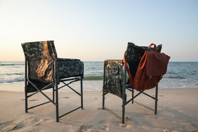 Camping chairs and backpack on sandy beach near sea