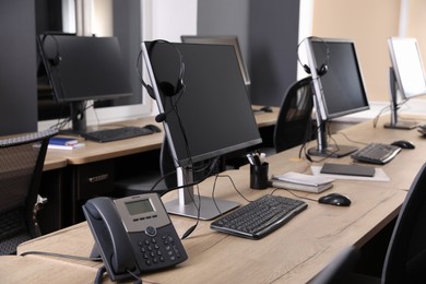 Photo of Modern computers with headsets and stationary phone on wooden desk in office. Hotline service