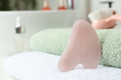 Rose quartz gua sha tool with towels on white countertop in bathroom, closeup. Space for text