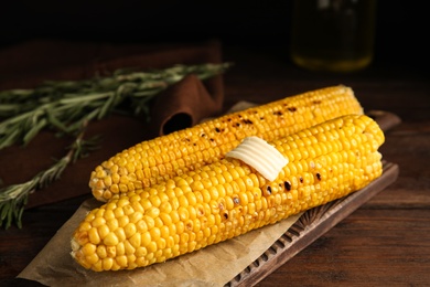 Photo of Fresh grilled corn cobs with butter on wooden table