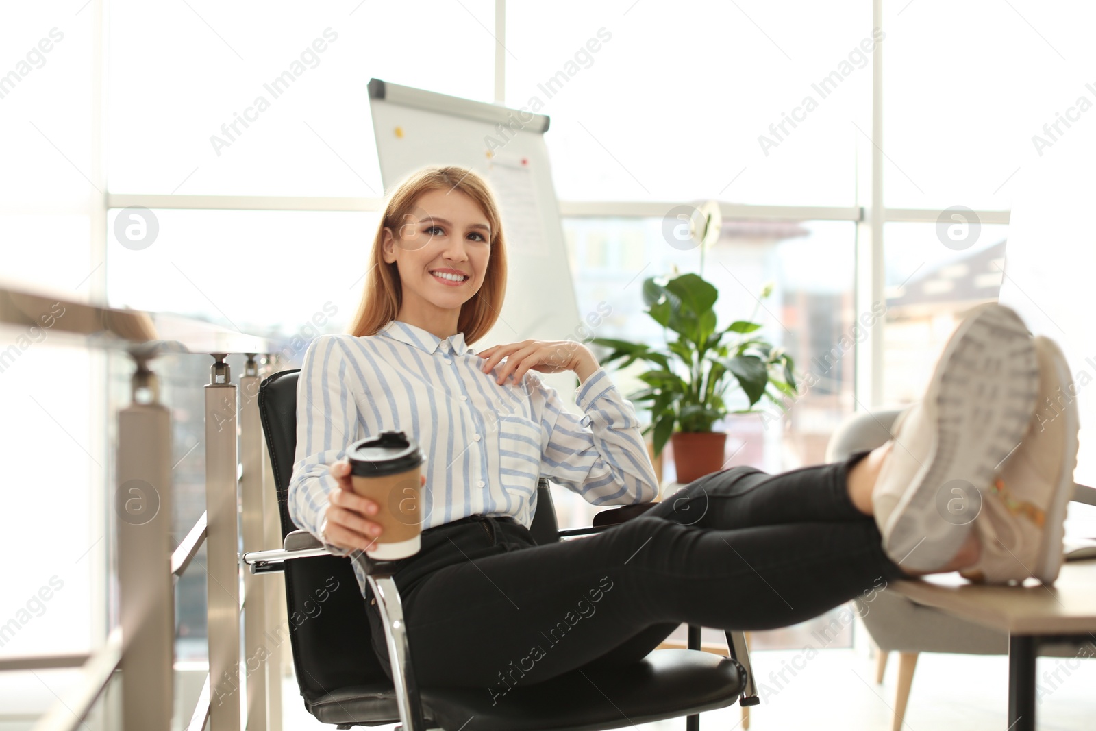 Photo of Young businesswoman with cup of coffee relaxing at table in office during break