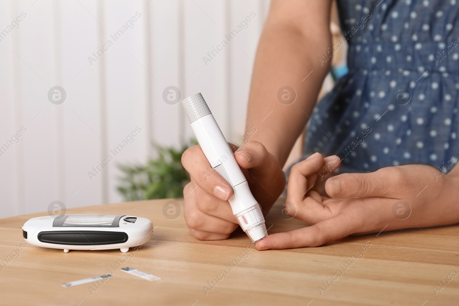 Photo of Woman using lancet pen at table. Diabetes test