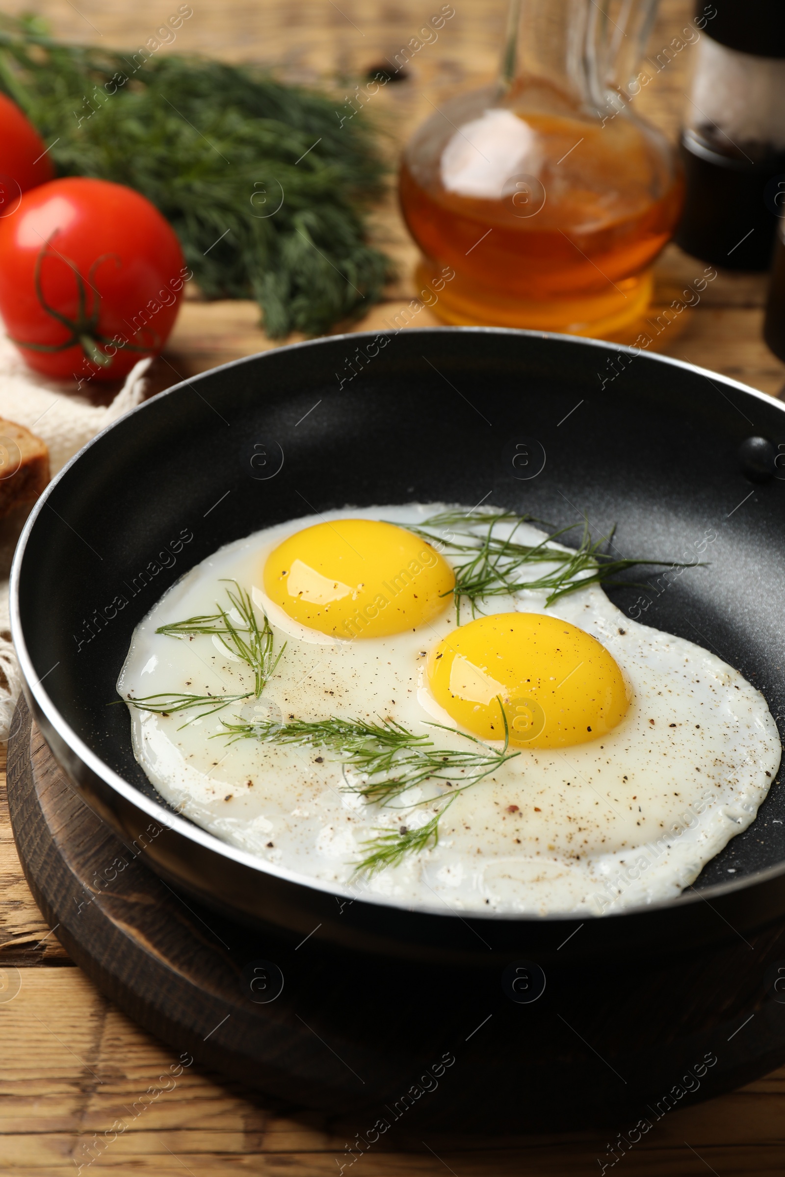 Photo of Frying pan with tasty cooked eggs, dill and other products on wooden table, closeup