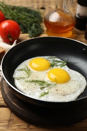 Photo of Frying pan with tasty cooked eggs, dill and other products on wooden table, closeup
