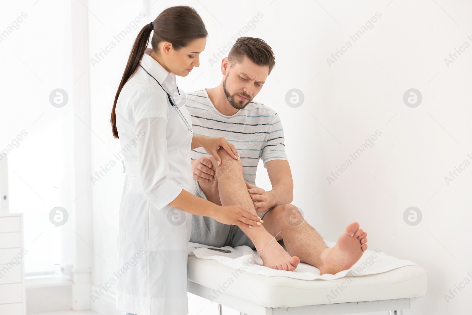 Photo of Doctor examining male patient with injured leg in clinic