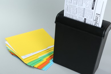 Shredder with sheet of paper and colorful folders on grey background