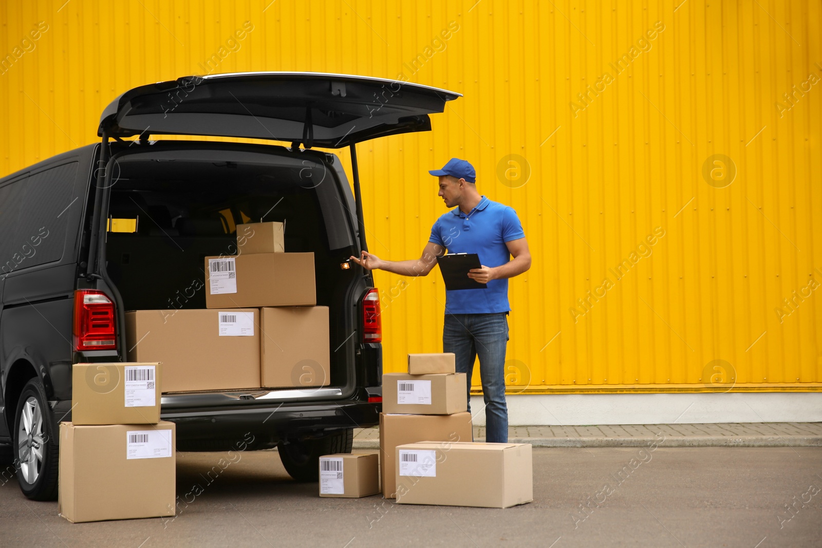 Photo of Courier with clipboard and parcels near delivery van outdoors