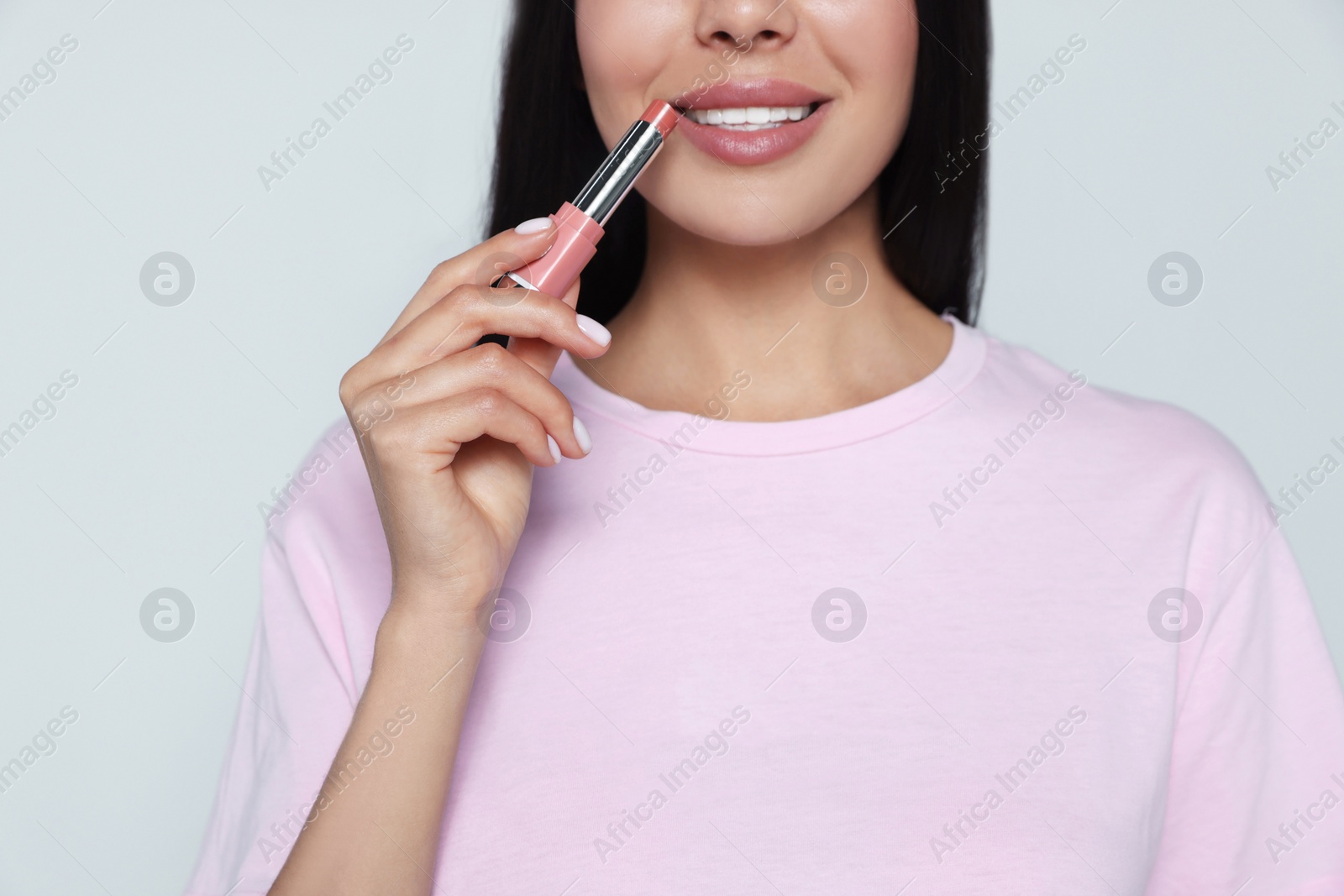 Photo of Young woman with beautiful makeup holding nude lipstick on light gray background, closeup