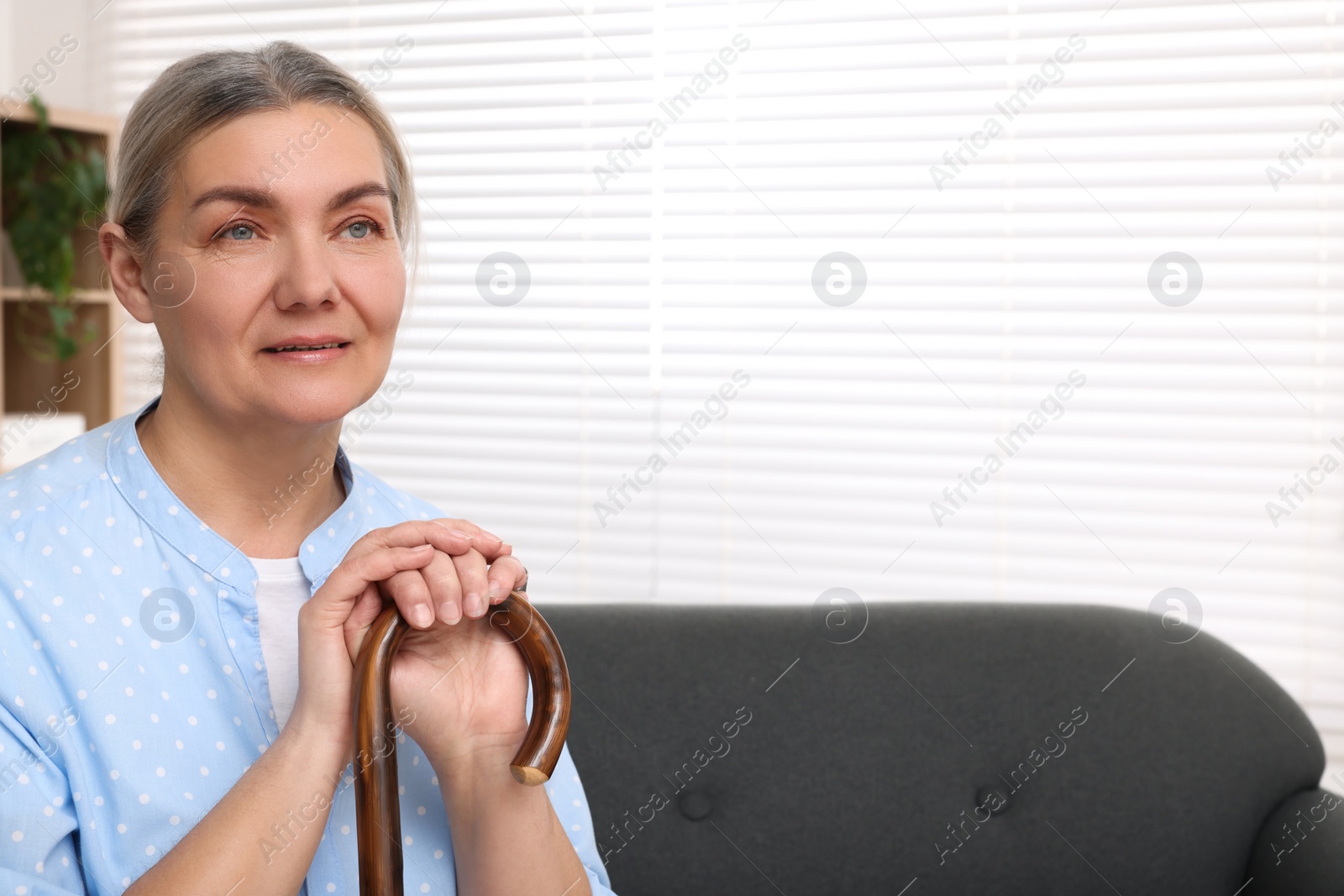 Photo of Senior woman with walking cane sitting on sofa at home. Space for text