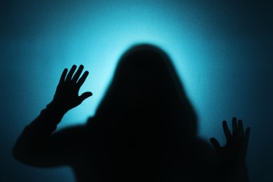 Silhouette of ghost behind glass against blue background