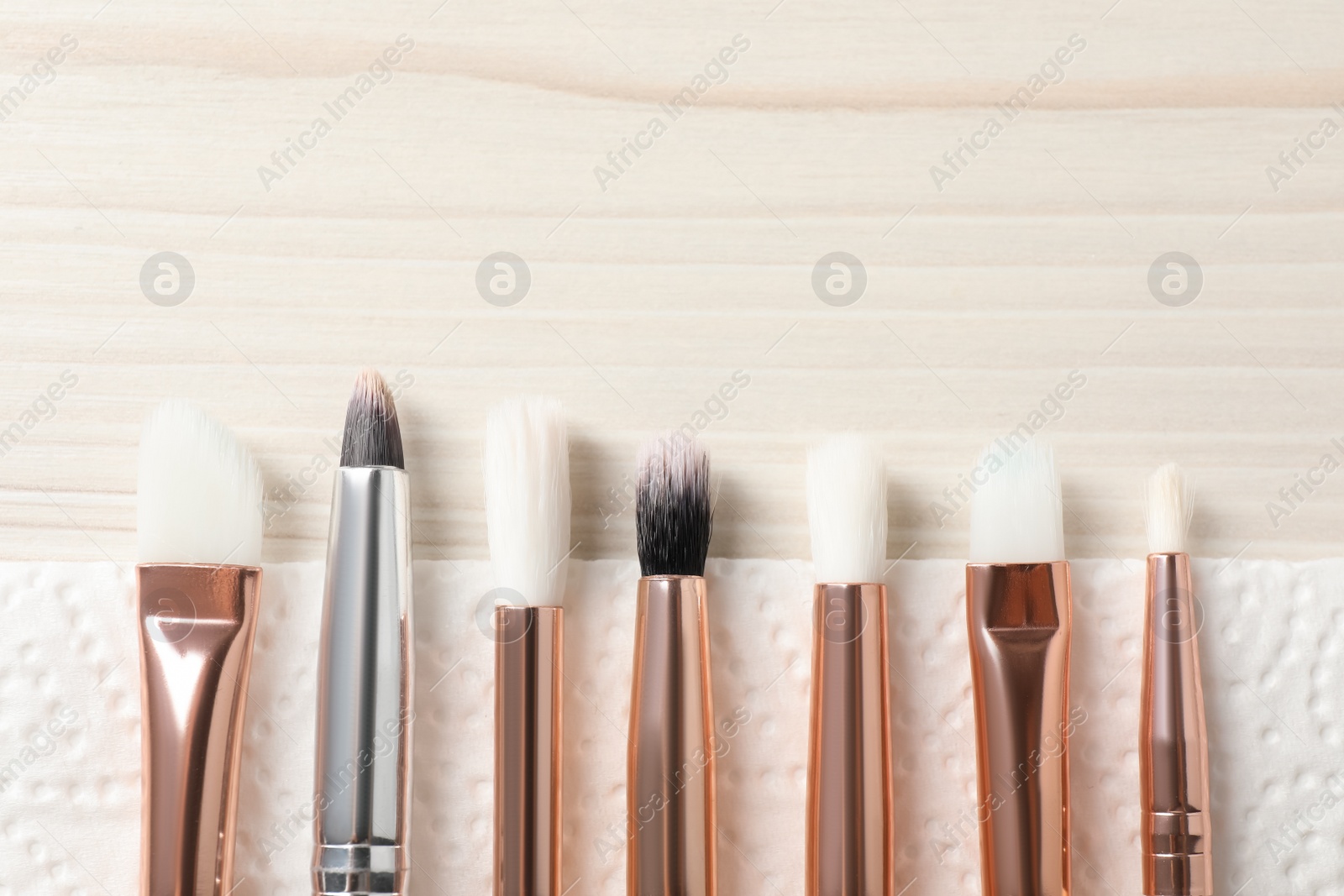 Photo of Set of different makeup brushes drying after cleaning on white wooden table, flat lay. Space for text