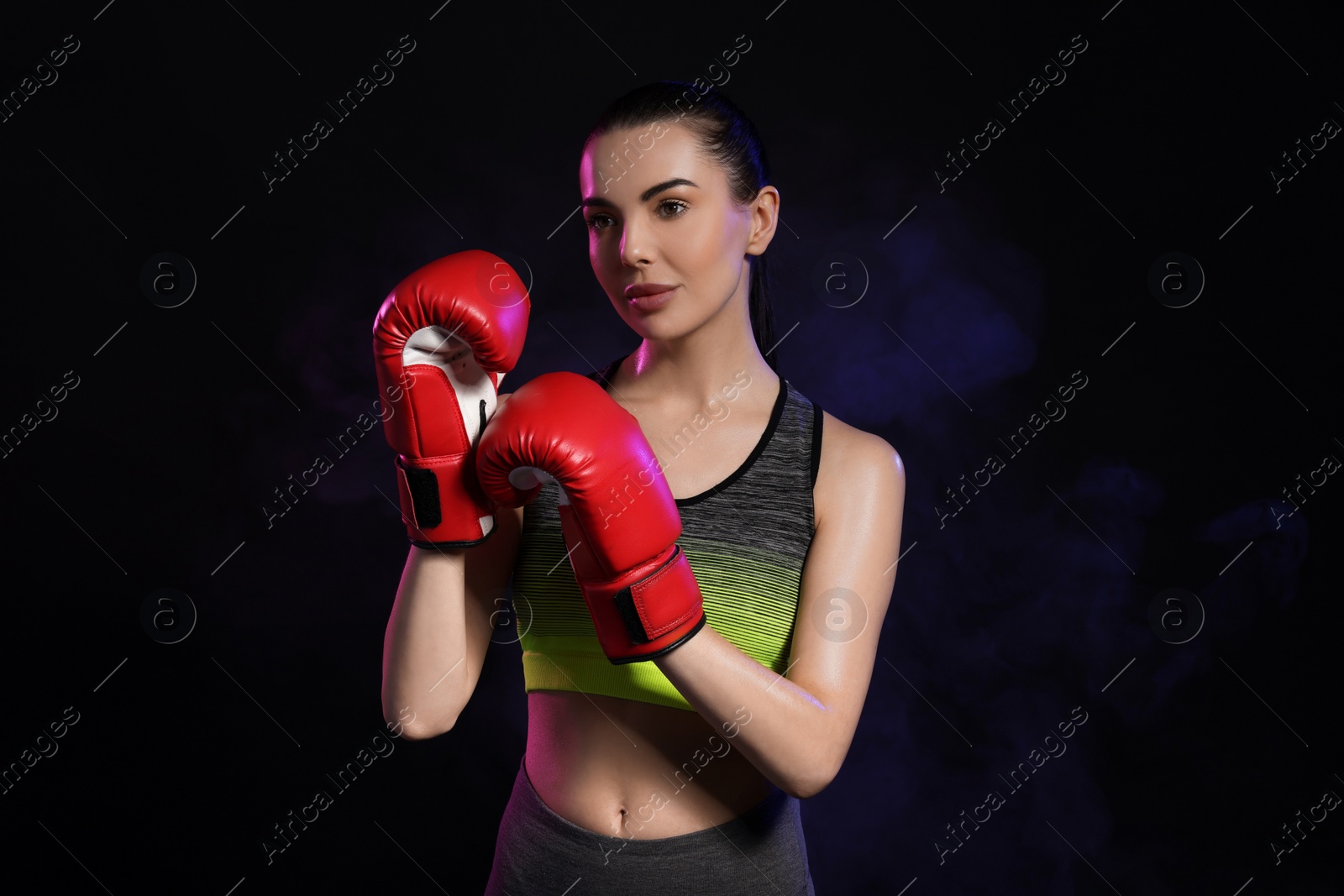 Photo of Portrait of beautiful woman wearing boxing gloves in color lights on black background