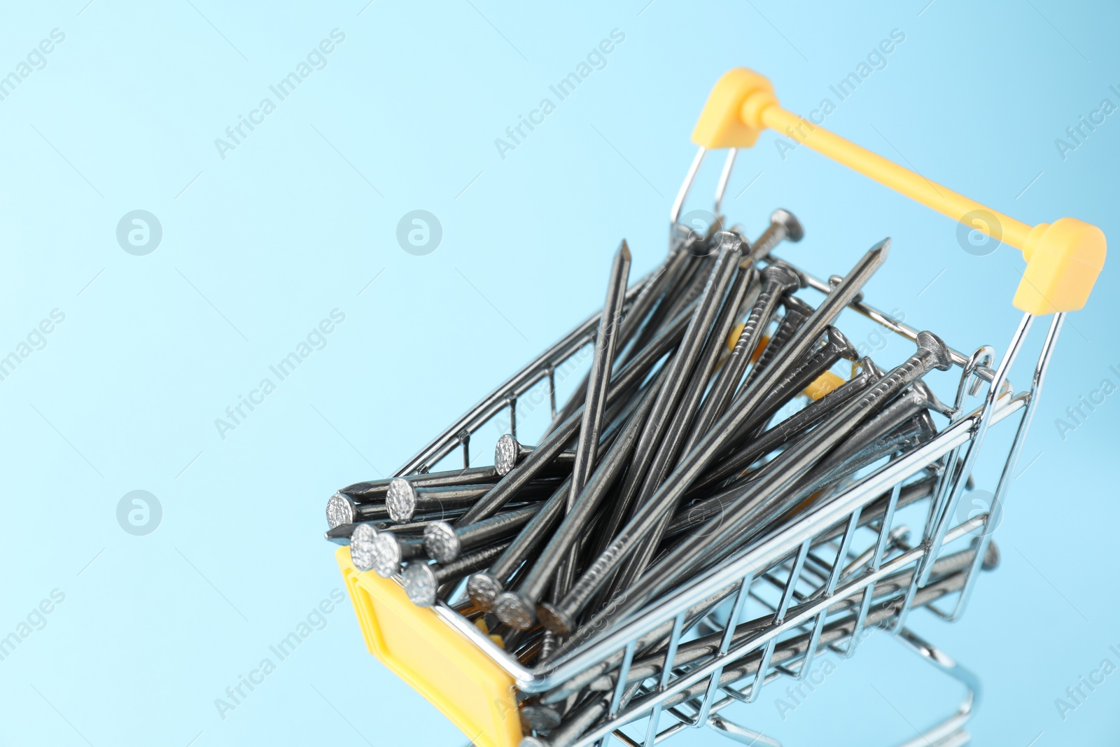 Photo of Metal nails in shopping cart on light blue background, closeup. Space for text