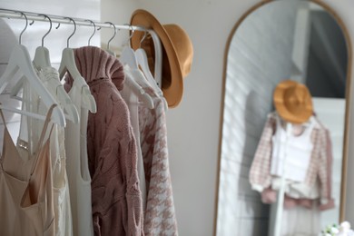 Photo of Rack with different stylish clothes and hat near mirror in dressing room, closeup