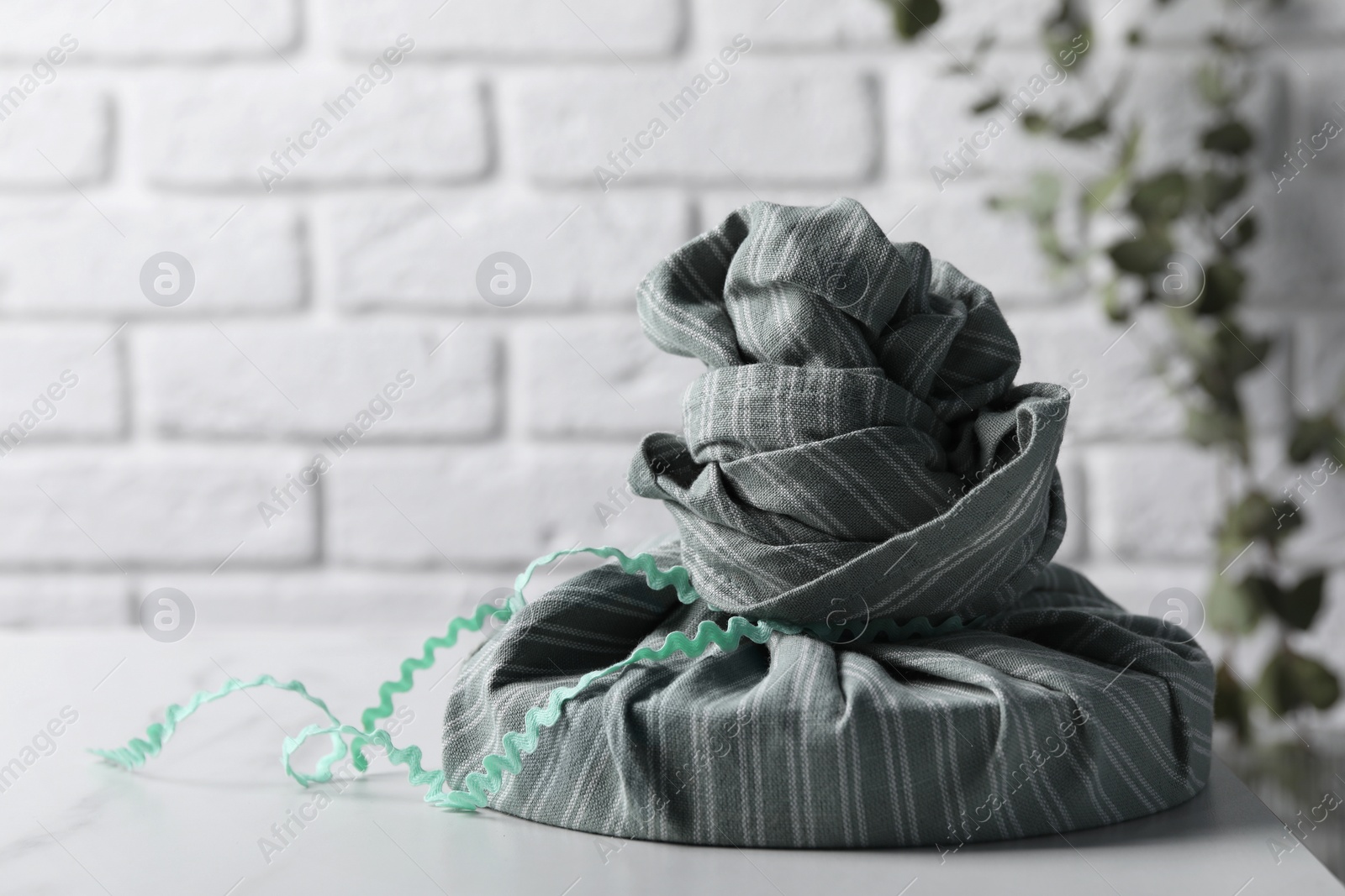 Photo of Furoshiki. Things packed in fabric and branch with green leaves on white table, space for text