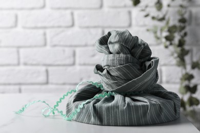 Furoshiki. Things packed in fabric and branch with green leaves on white table, space for text