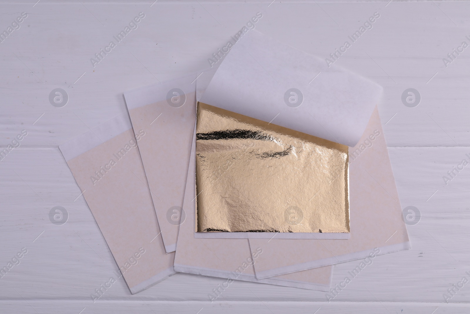 Photo of Many edible gold leaf sheets on white wooden table, flat lay