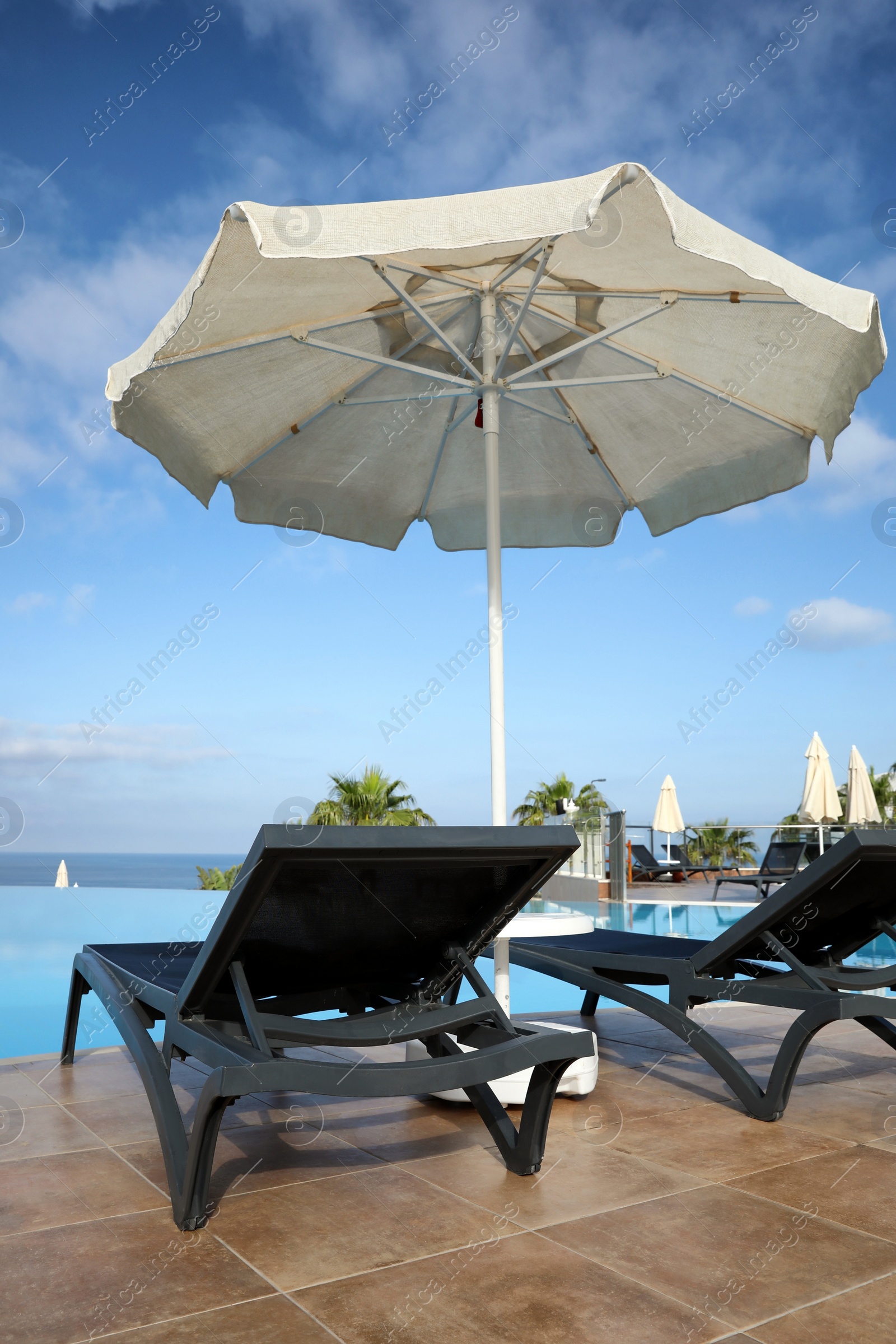 Photo of Chaise longues and beach parasol near infinity pool at resort