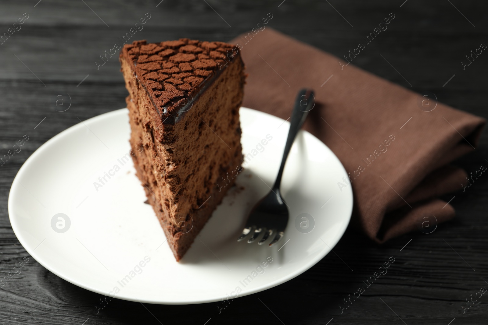 Photo of Piece of delicious chocolate truffle cake and fork on black wooden table, closeup