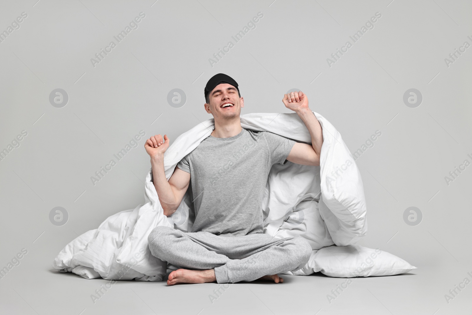 Photo of Happy man in pyjama and sleep mask wrapped in blanket on grey background