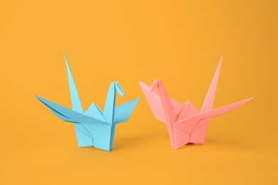 Origami art. Beautiful light blue and pale pink paper cranes on orange background