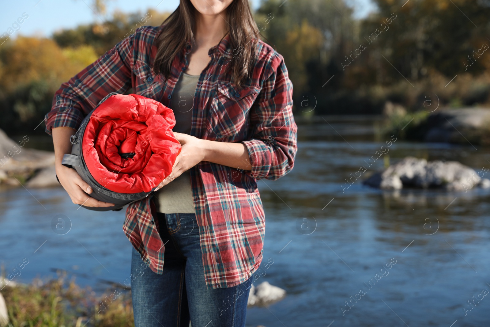 Photo of Female camper with sleeping bag near pond. Space for text