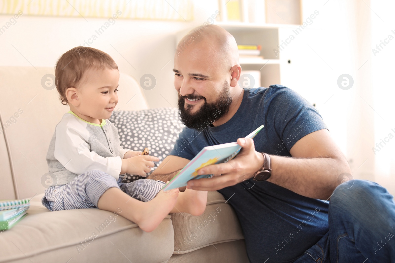 Photo of Dad reading book with his little son in living room