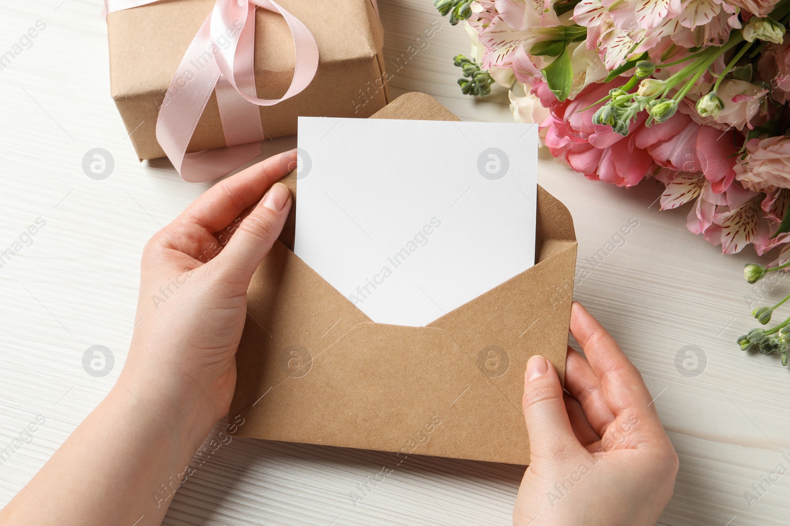 Photo of Happy Mother's Day. Woman holding envelope with blank card at white wooden table, top view