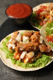 Photo of Delicious tacos with vegetables, meat and ketchup on grey textured table, closeup