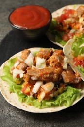 Delicious tacos with vegetables, meat and ketchup on grey textured table, closeup