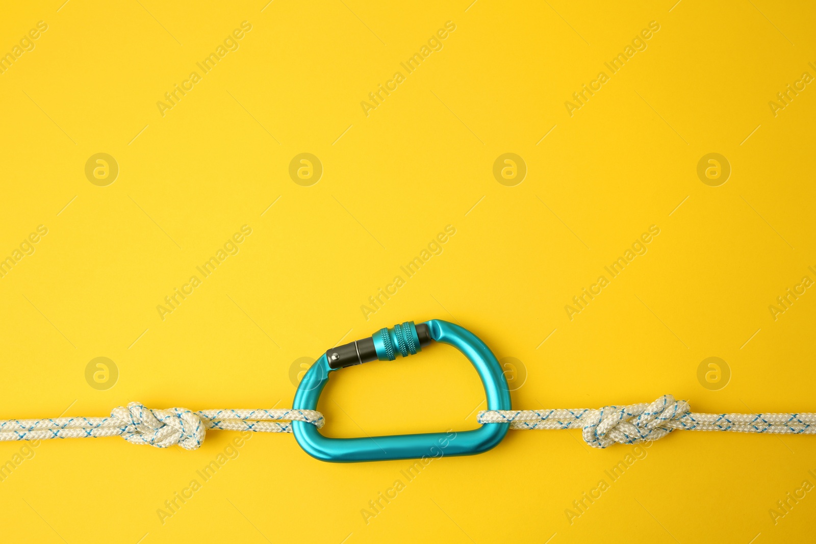 Photo of One metal carabiner with ropes on yellow background, top view. Space for text