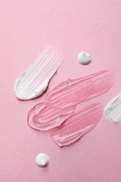 Samples of cosmetic gel and cream on pink background, top view