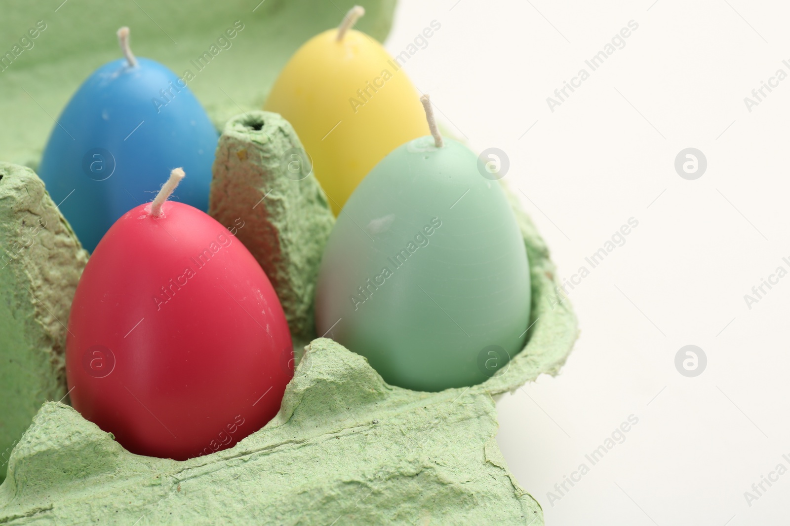 Photo of Colorful egg shaped candles in carton on white table, closeup. Easter decor