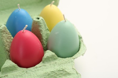 Photo of Colorful egg shaped candles in carton on white table, closeup. Easter decor