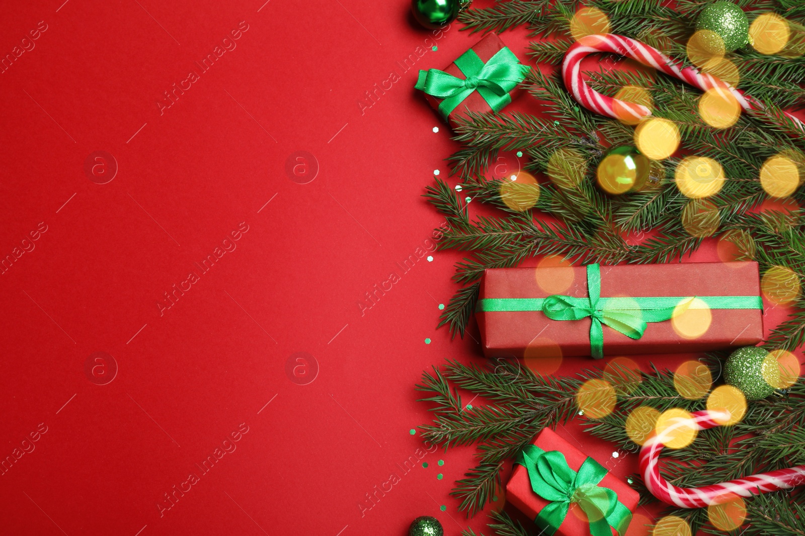 Photo of Flat lay composition with fir tree branches, Christmas decor and gift boxes on red background, space for text. Bokeh effect