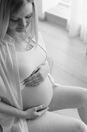 Photo of Beautiful pregnant woman sitting in room at home, black and white effect