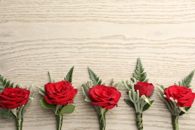 Many stylish red boutonnieres on light wooden table, flat lay. Space for text