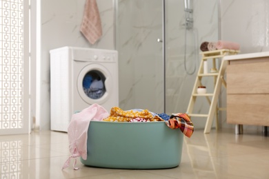 Photo of Plastic laundry basket full of different clothes on floor in bathroom