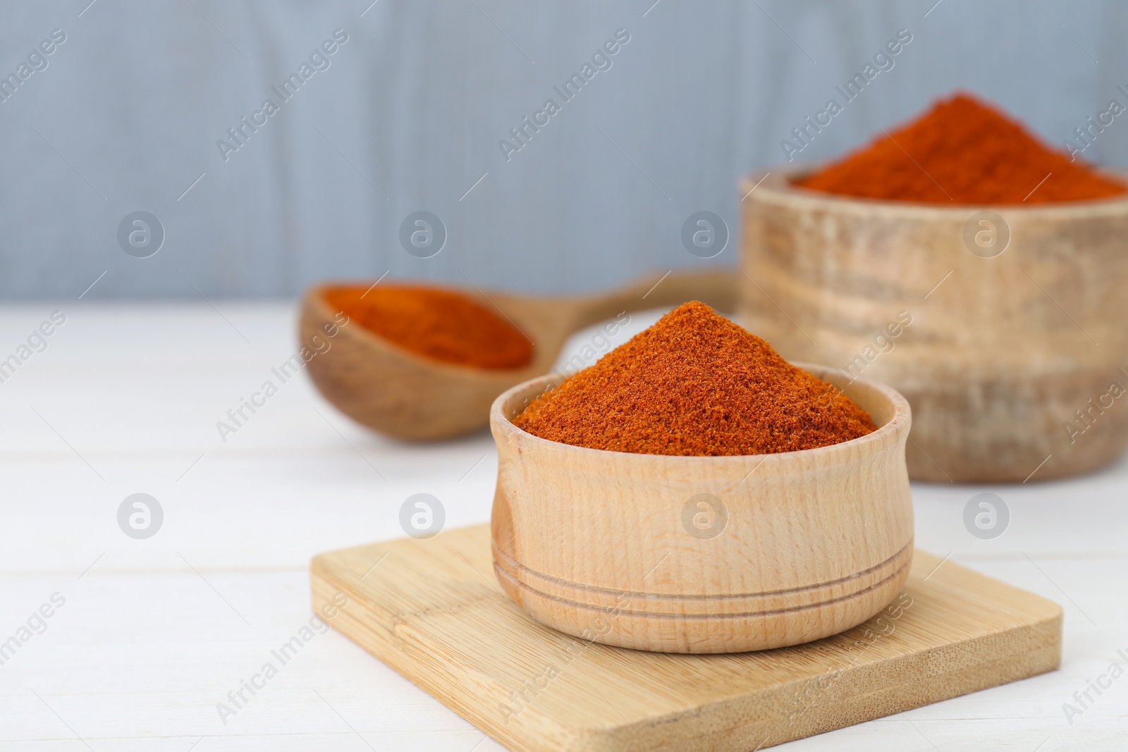 Photo of Bowls and spoon with aromatic paprika powder on white table. Space for text