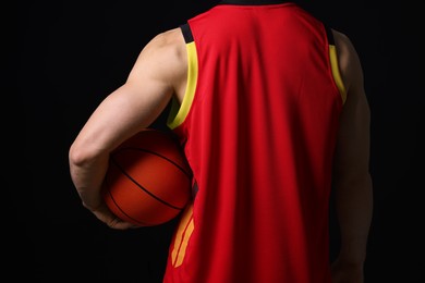 Athletic man with basketball ball on black background, closeup