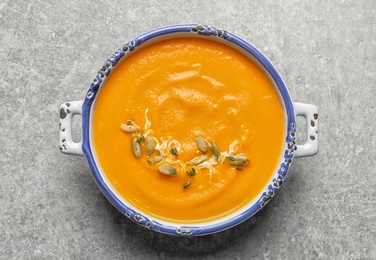 Photo of Bowl with tasty pumpkin soup on gray background, top view