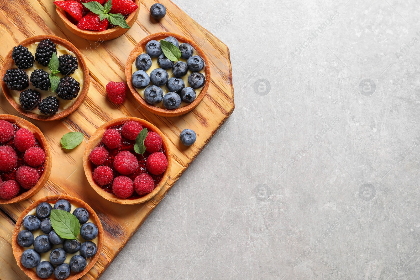 Photo of Tartlets with different fresh berries on light grey table, top view and space for text. Delicious dessert