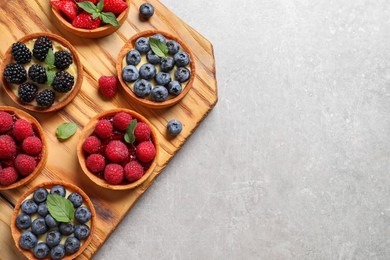 Tartlets with different fresh berries on light grey table, top view and space for text. Delicious dessert