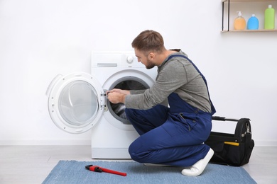 Young plumber fixing washing machine in bathroom