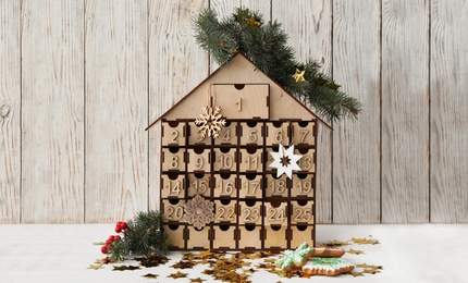 Photo of Wooden house shaped advent calendar, Christmas cookies and festive decor on white table